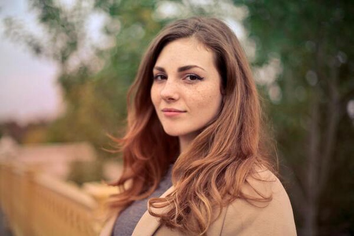 The woman wears a brown coat and a gray top