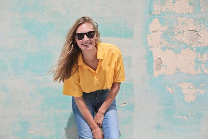 Woman in yellow polo shirt stands in front of a blue-green concrete wall