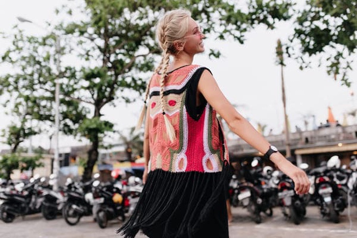 Laughing woman with long blonde braids. Outdoor shot of graceful tanned woman wears colorful knitted clothes.