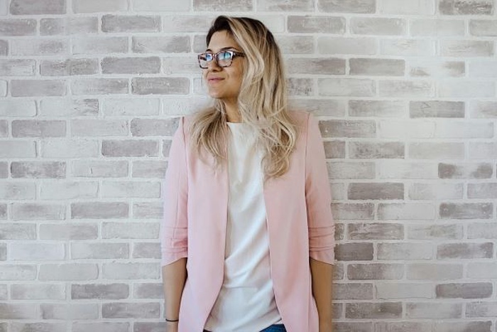 Pink cardigan and white shirt, woman leaning against the wall